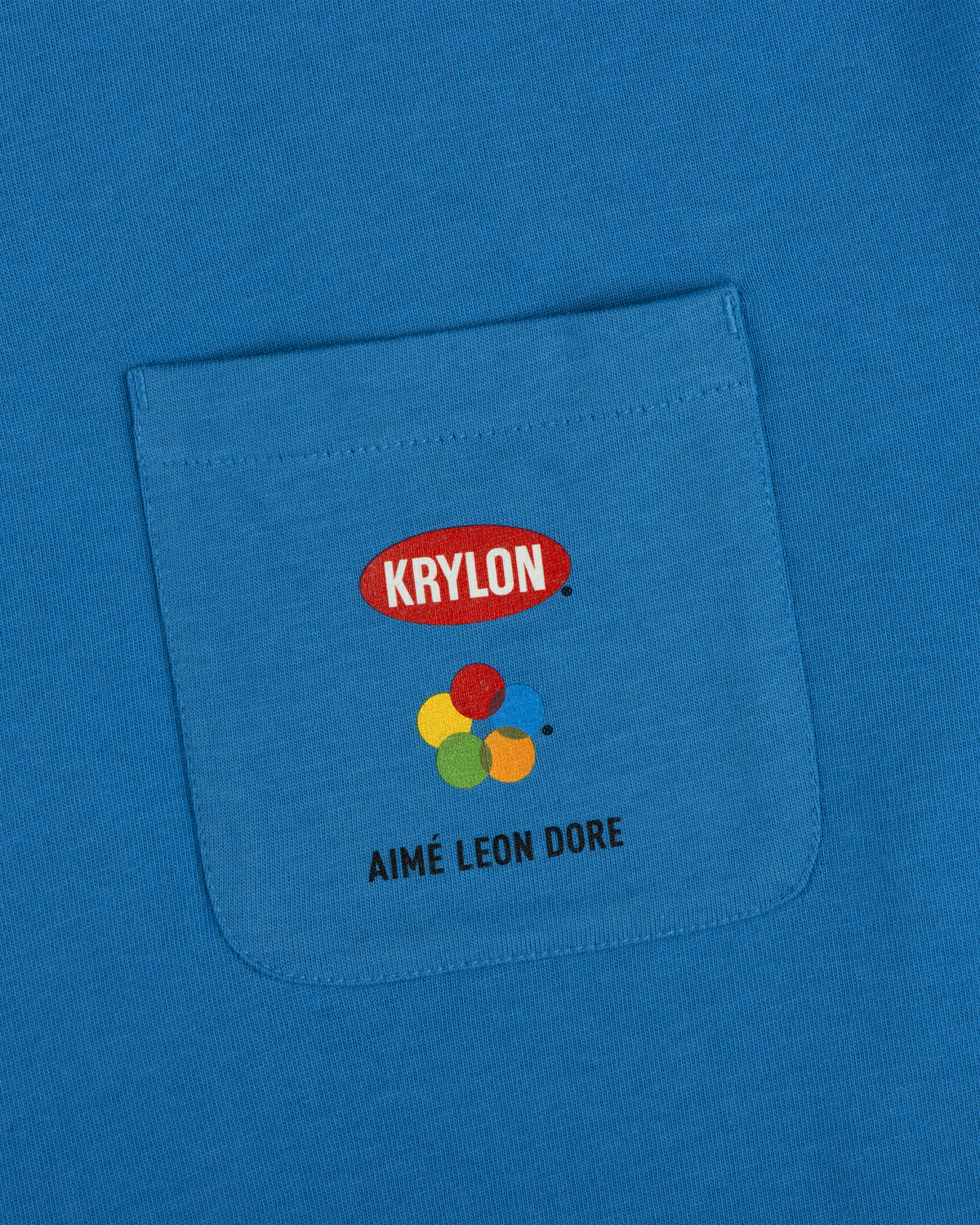 Krylon Pocket Tee features a blue pocket with four paint circles and AIMÉ LEON DORE printed on the front.