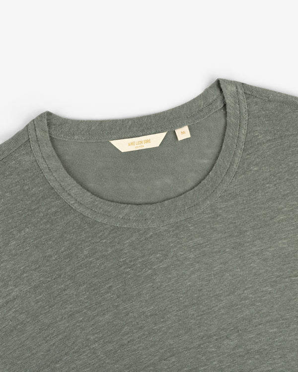 A close-up of a sage green Long-Sleeve Linen Tee with a beige size tag labeled M.