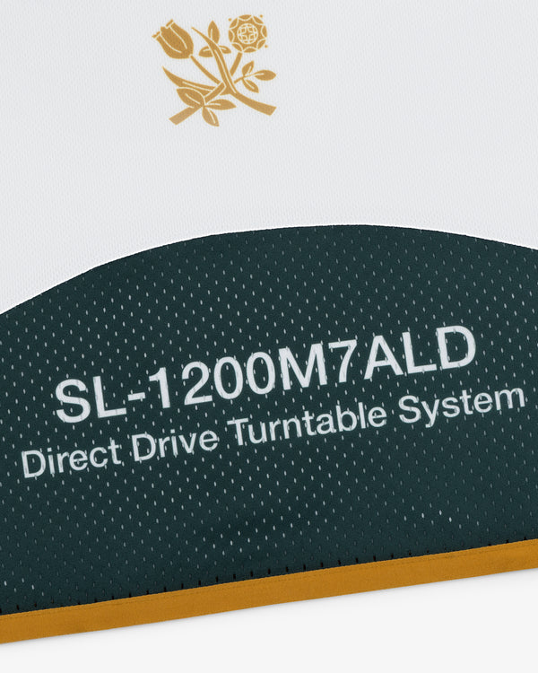 Close-up of text reading ALD / Technics Soccer Jersey on a dark, textured surface with gold trim and logo.