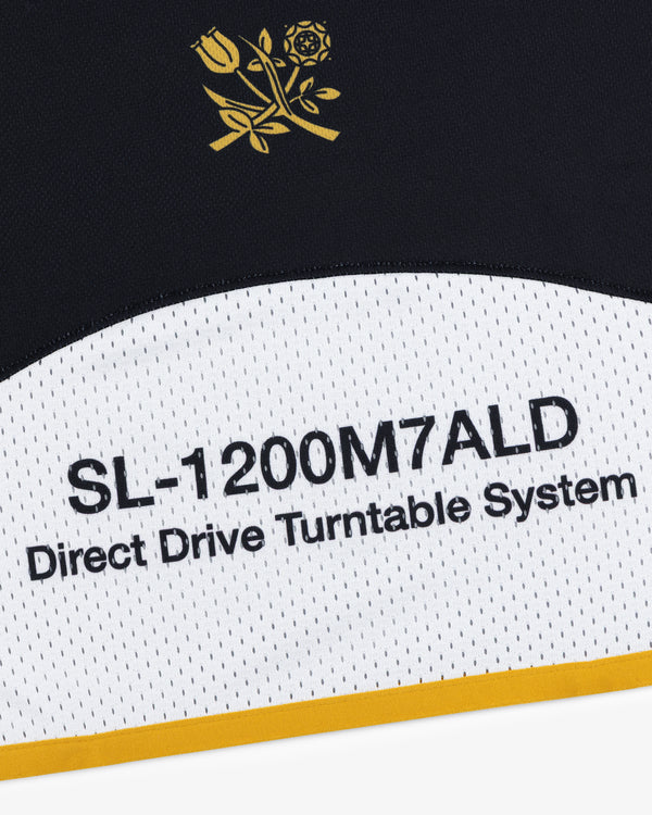 Close-up of ALD / Technics Soccer Jersey text on a white and black surface with a gold border.