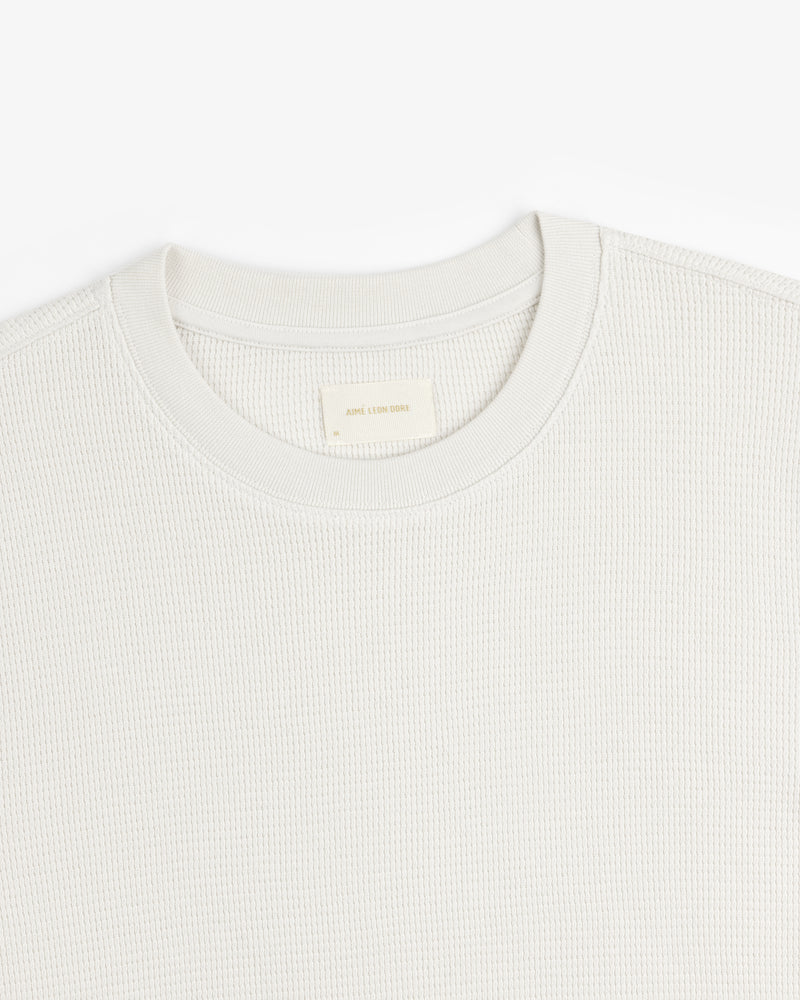 Close-up of a textured, light-colored Long-Sleeve Waffle Thermal crew neck with visible neck label on white background.