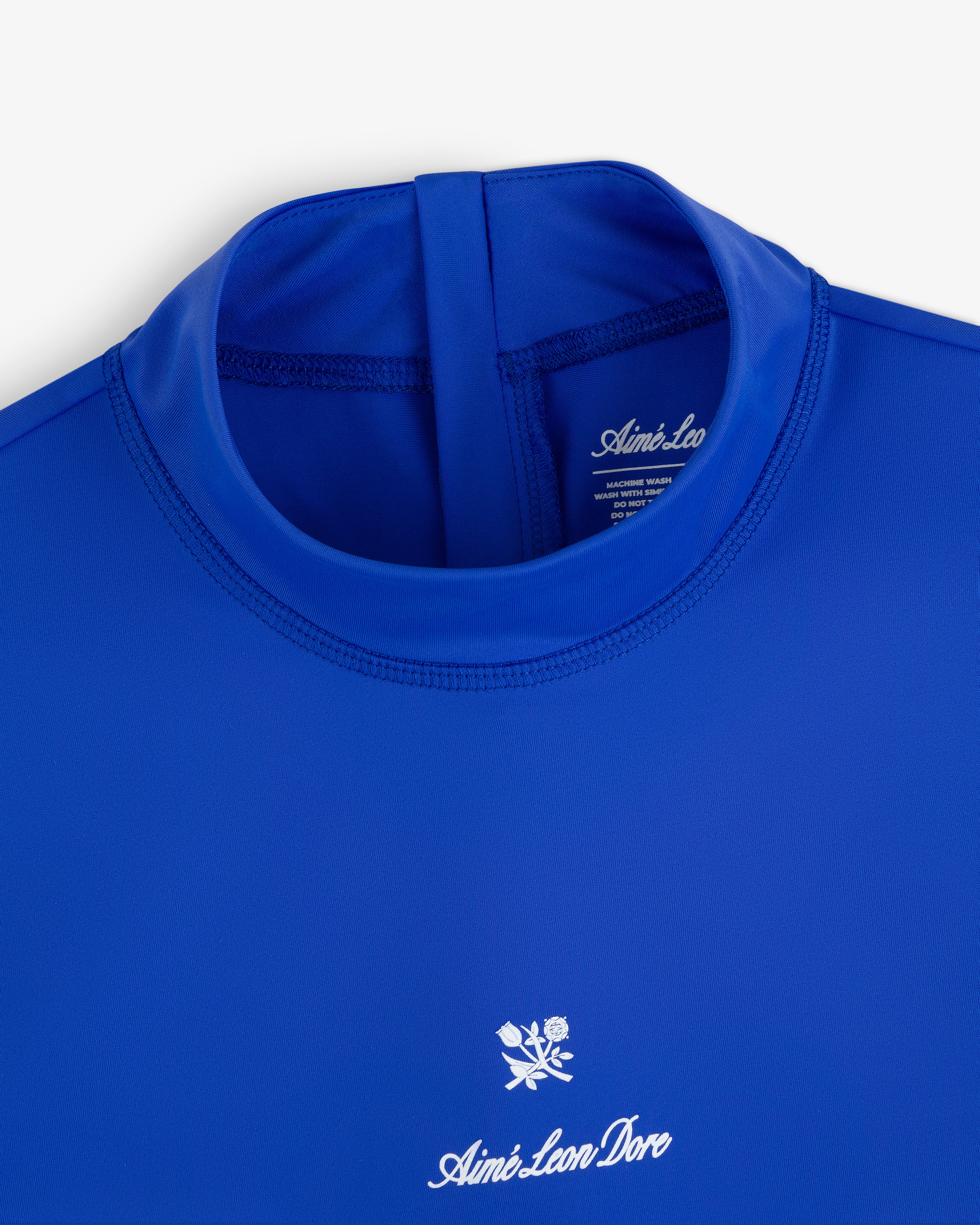 Close-up of the Short Sleeve Crest Rash Guard in royal blue with “Aimé Leon Dore” logo and white rose chest emblem.