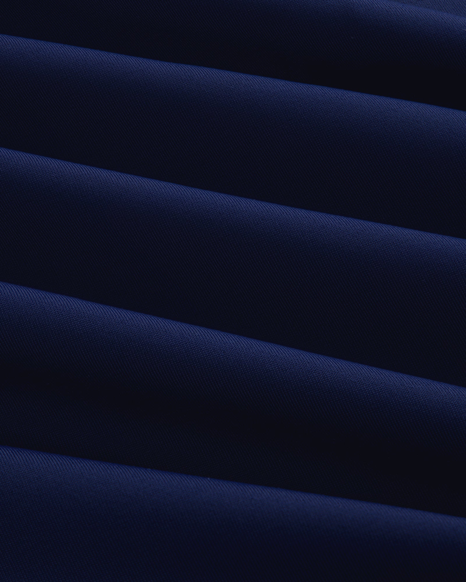 Close-up of Short Sleeve Crest Rash Guard in dark blue with diagonal folds creating light and shadow patterns.