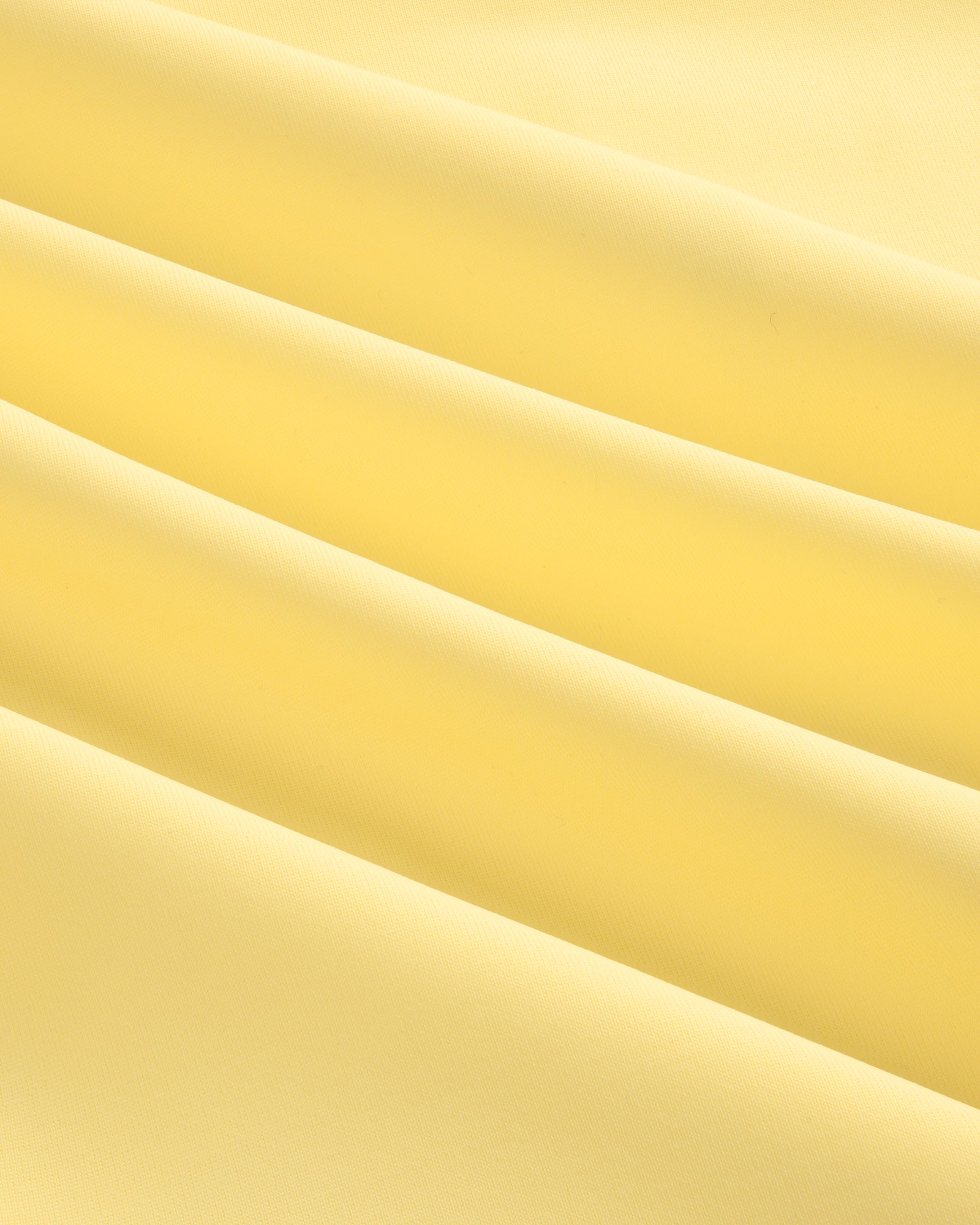 Close-up of smooth, light yellow Short Sleeve Crest Rash Guard fabric with soft, diagonal folds and gentle shadows.