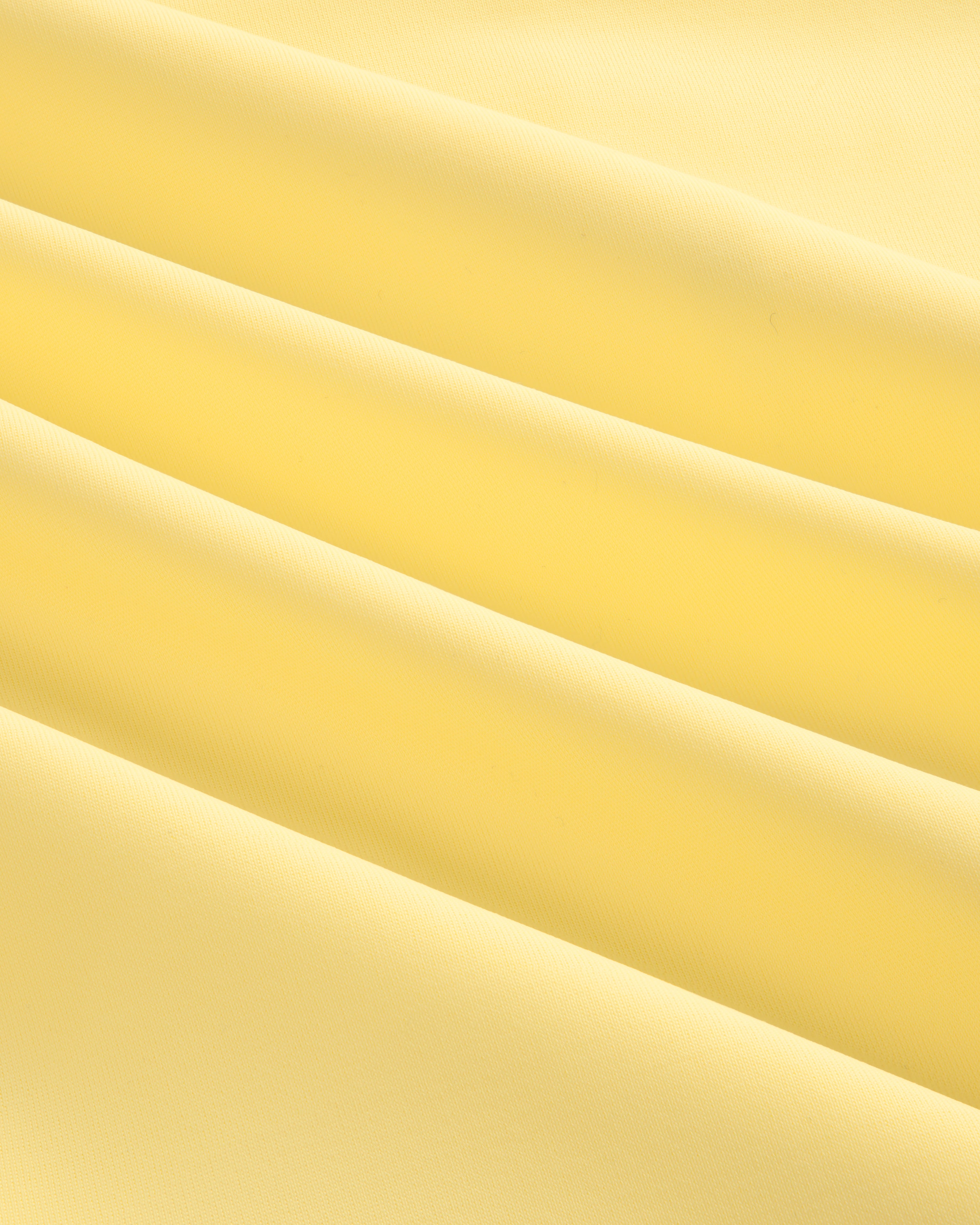Close-up of smooth, light yellow Short Sleeve Crest Rash Guard fabric with soft, diagonal folds and gentle shadows.