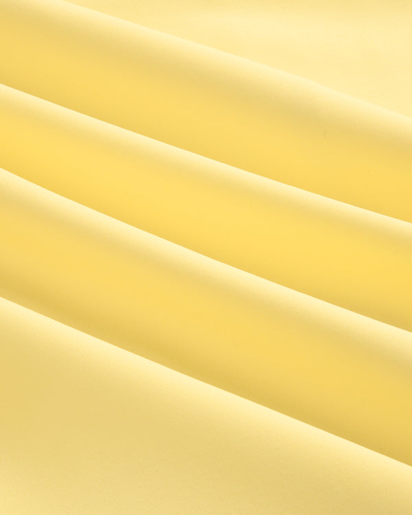 Close-up of smooth, light yellow Short Sleeve Crest Rash Guard fabric with soft, diagonal folds and gentle shadows.
