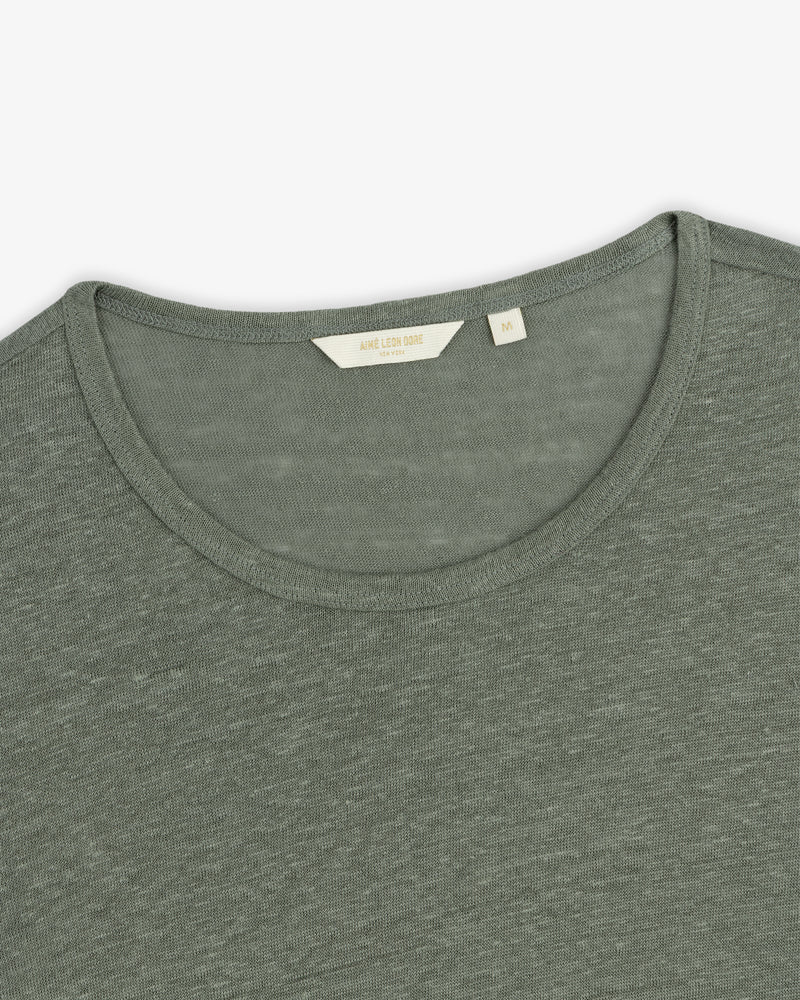 Close-up of a sage green Linen Tee with a small beige size label visible inside the crew neckline.
