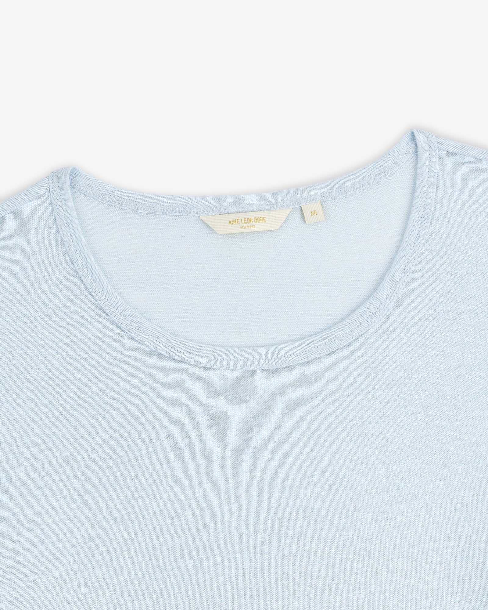 Linen Tee in light blue with a cream-colored label inside the collar, shown on a white background.