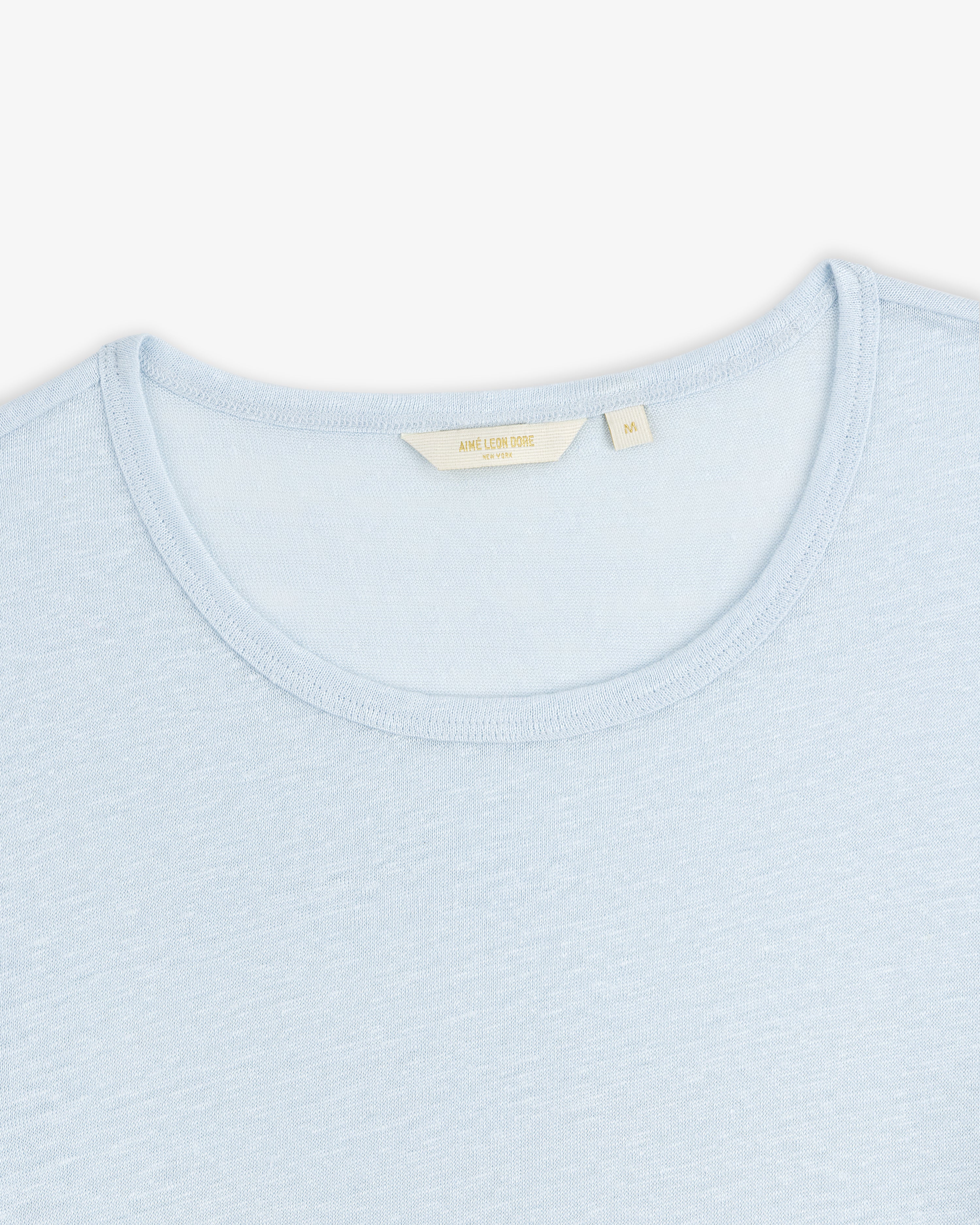 Linen Tee in light blue with a cream-colored label inside the collar, shown on a white background.