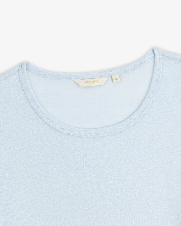 Linen Tee in light blue with a cream-colored label inside the collar, shown on a white background.