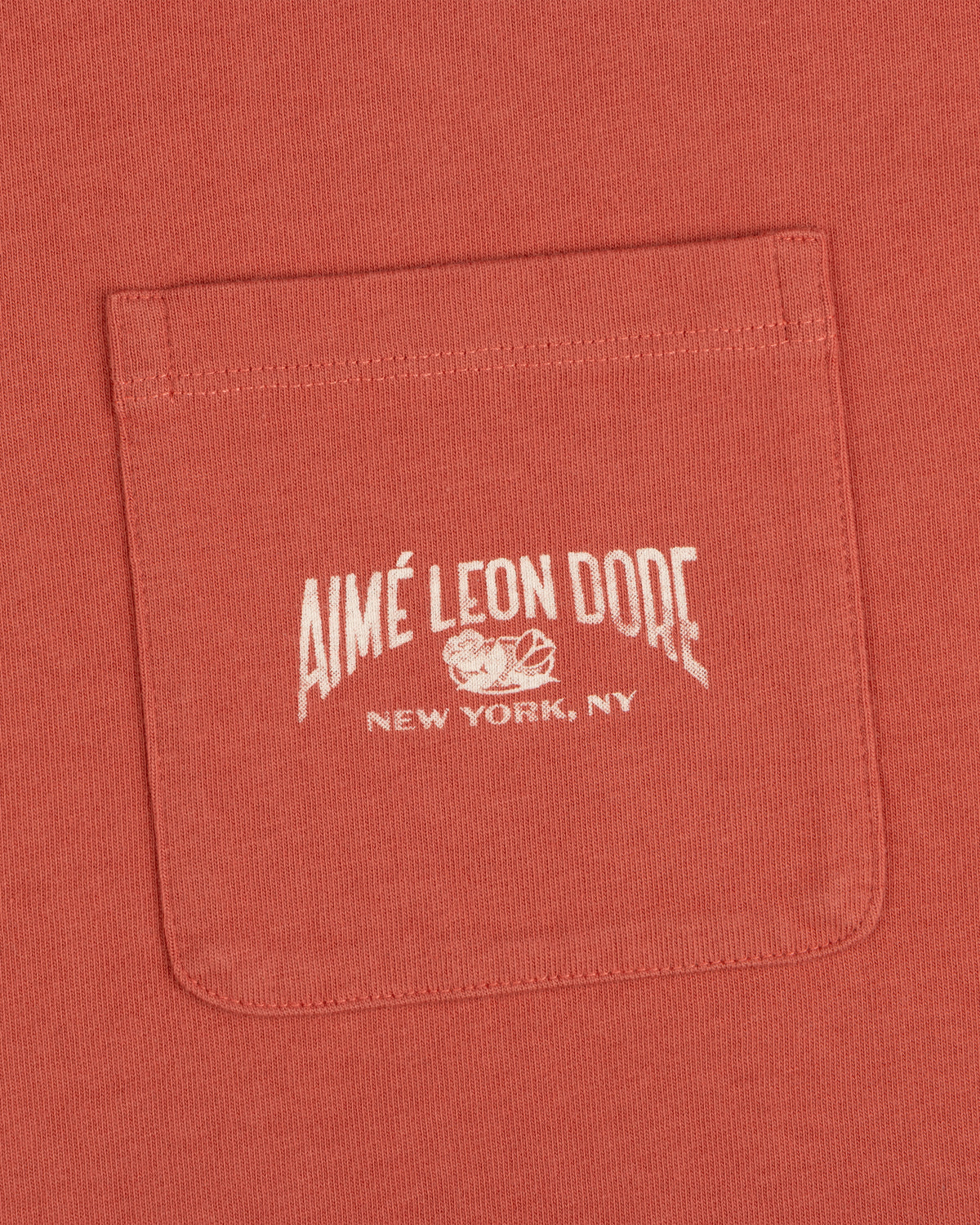 Neighborhood Pocket Tee in red features a pocket with white "Aimé Leon Dore New York, NY" text and a small logo above.