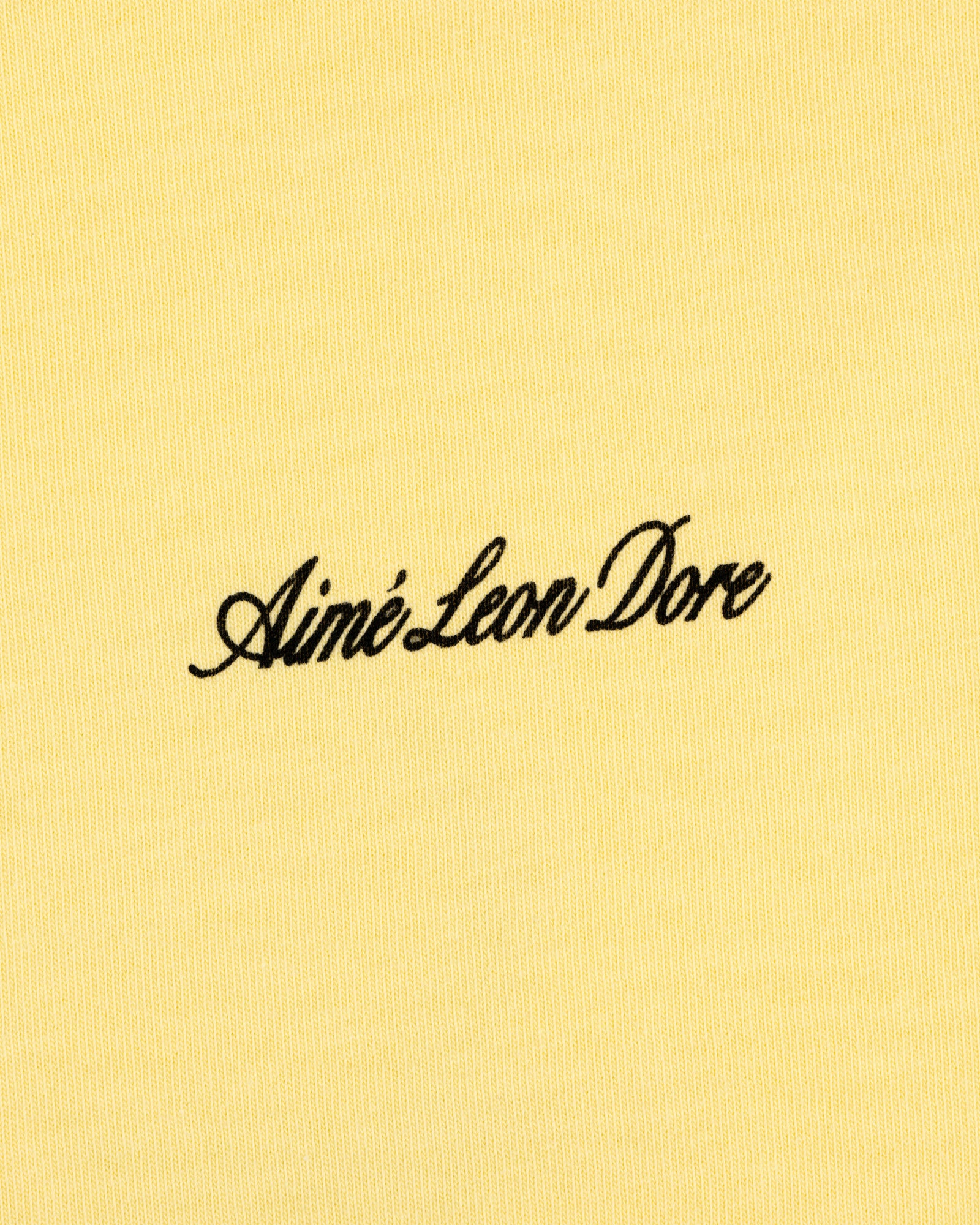 Yellow Super Cub Tee with Aimé Leon Dore in black cursive text at the center.