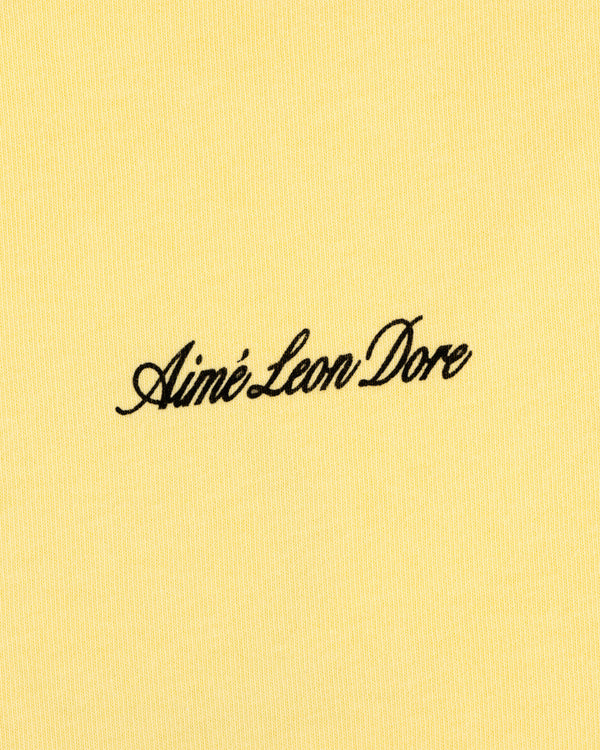 Yellow Super Cub Tee with Aimé Leon Dore in black cursive text at the center.