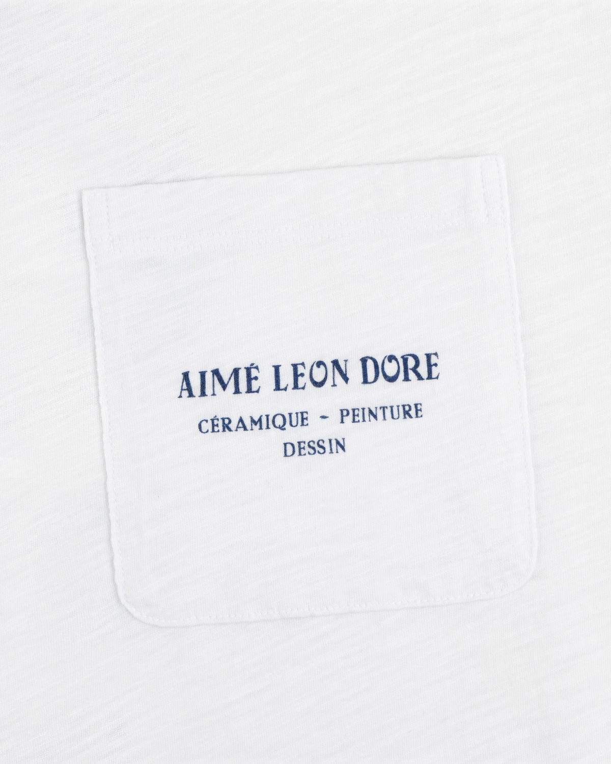White Artiste Pocket Tee with blue text: AIMÉ LEON DORE CÉRAMIQUE - PEINTURE DESSIN.