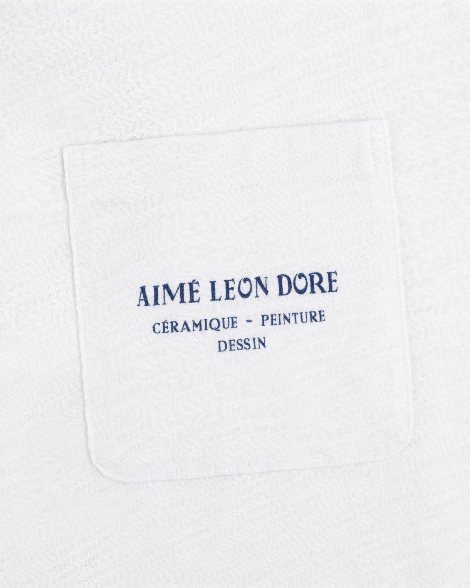 White Artiste Pocket Tee with blue text: AIMÉ LEON DORE CÉRAMIQUE - PEINTURE DESSIN.
