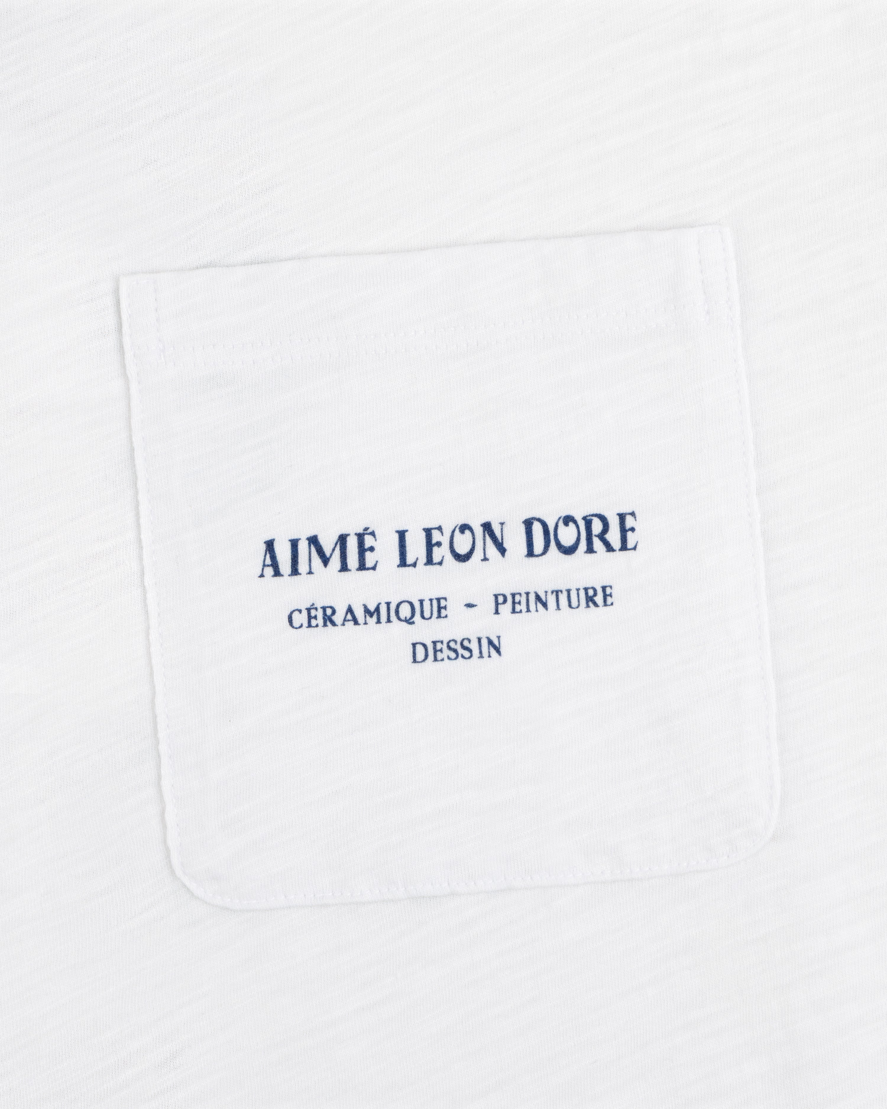 White Artiste Pocket Tee with blue text: AIMÉ LEON DORE CÉRAMIQUE - PEINTURE DESSIN.