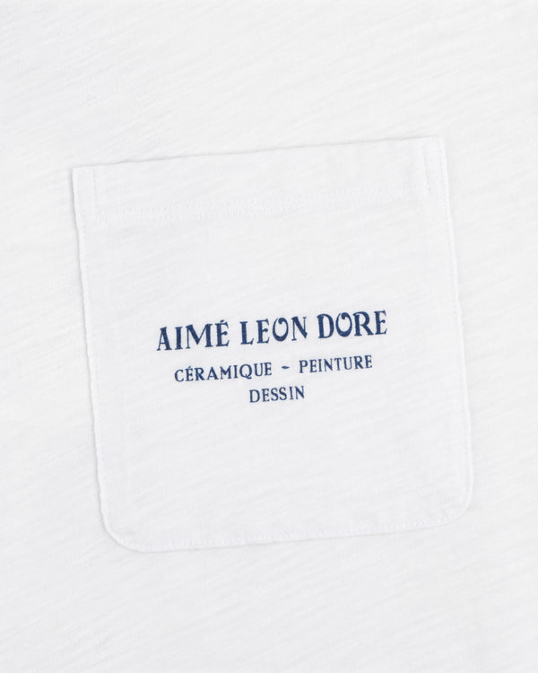 White Artiste Pocket Tee with blue text: AIMÉ LEON DORE CÉRAMIQUE - PEINTURE DESSIN.