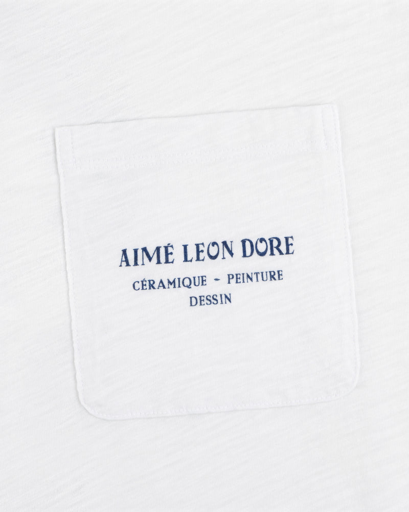 White Artiste Pocket Tee with blue text: AIMÉ LEON DORE CÉRAMIQUE - PEINTURE DESSIN.