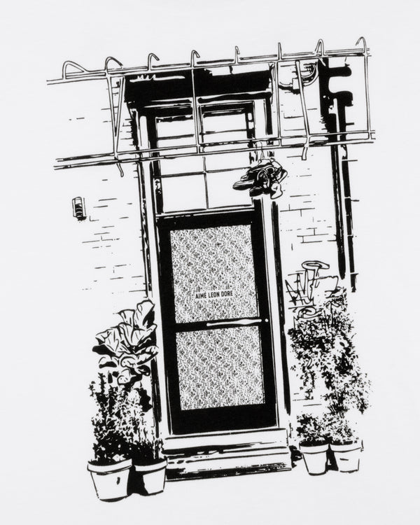 Black and white illustration of a door with "Mott Street Tee," potted plants by the entrance, and a metal awning above.