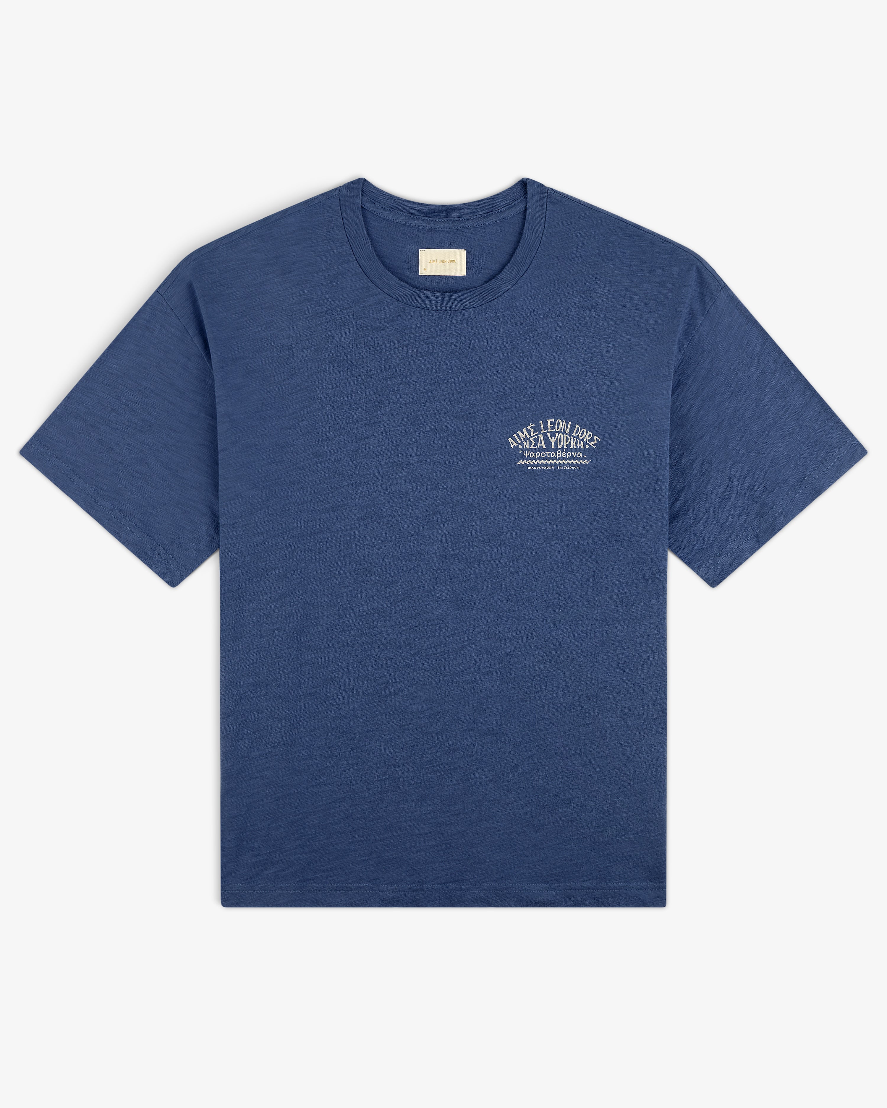 Taverna Tee in blue, short sleeves, with small white text logo on left chest, laid flat on white background.