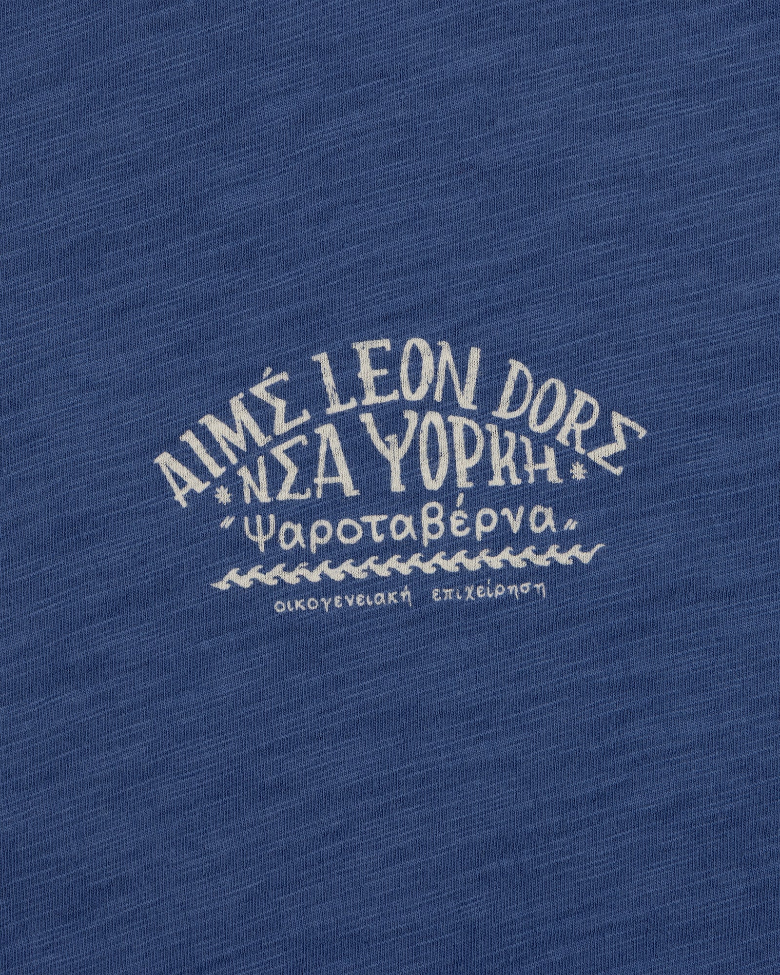 Greek and English text printed on blue Taverna Tee, featuring "AIMÉ LEON DORE NEW YORK.