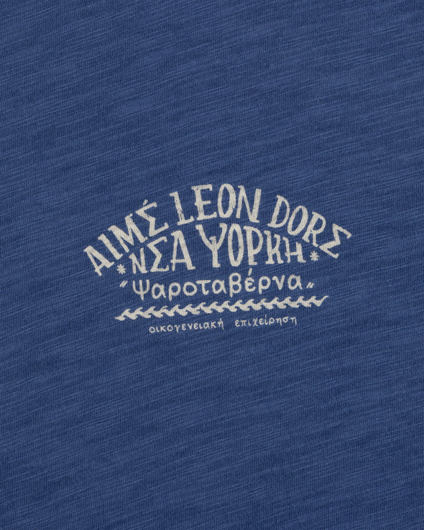 Greek and English text printed on blue Taverna Tee, featuring "AIMÉ LEON DORE NEW YORK.