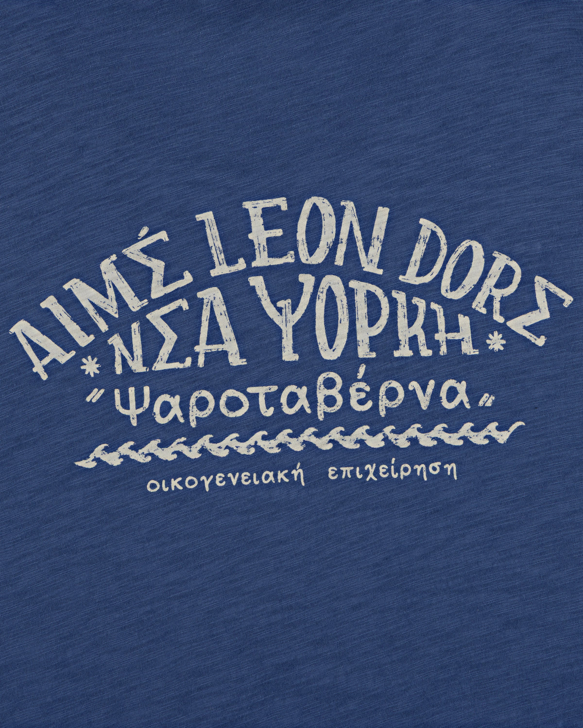White Greek-style text on blue reads “AIMS LEON DORE Νέα Υόρκη” on the Taverna Tee.