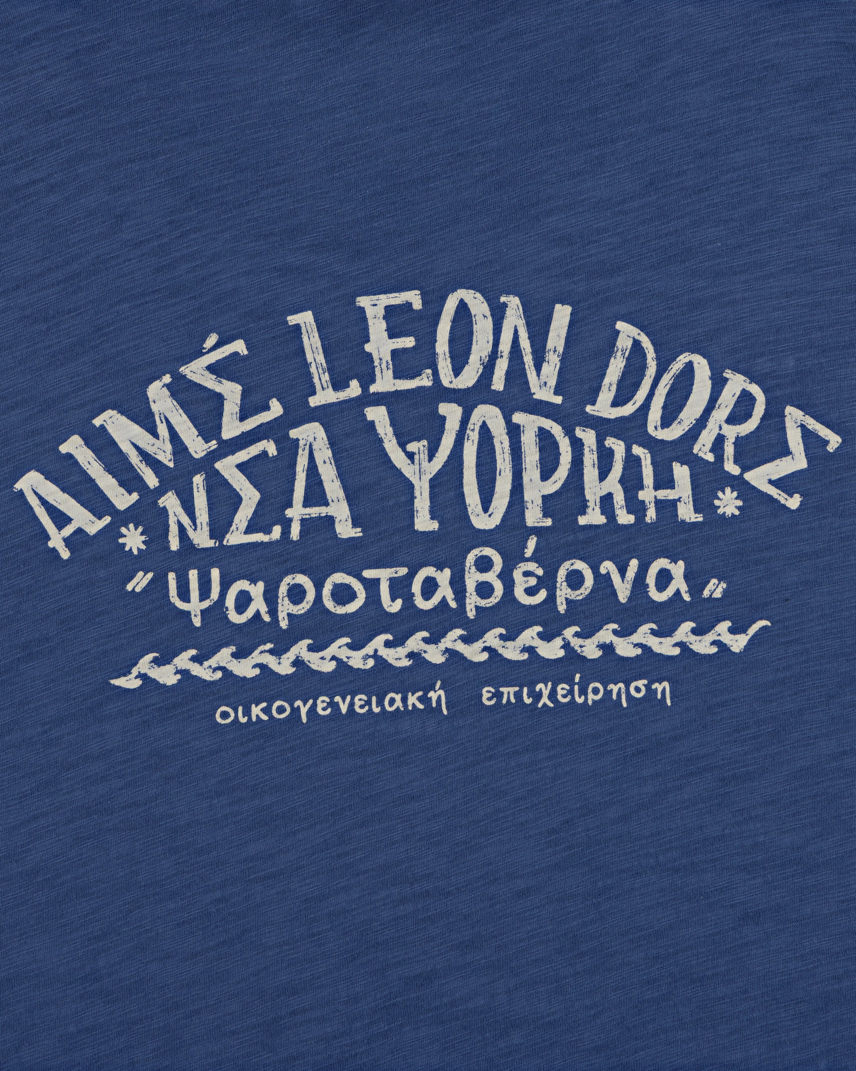 White Greek-style text on blue reads “AIMS LEON DORE Νέα Υόρκη” on the Taverna Tee.