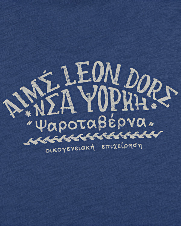 White Greek-style text on blue reads “AIMS LEON DORE Νέα Υόρκη” on the Taverna Tee.