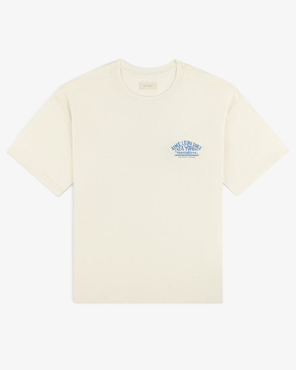 Taverna Tee: Cream short-sleeve shirt with small blue text and graphic on left chest.