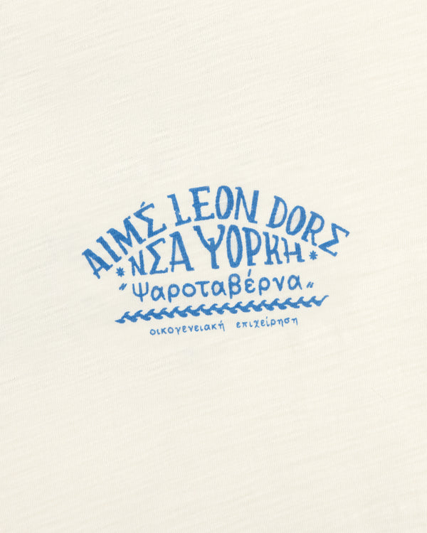 White Taverna Tee with blue Greek & English text: AIMÉ LEON DORE ΝΕΑ ΥΟΡΚΗ Ψαροταβέρνα οικογενειακή επιχείρηση.