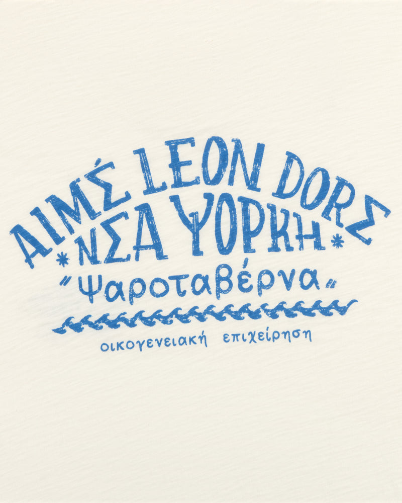 Blue Greek-style text on a white tee reads Aimé Leon Dore Νέα Υόρκη Ψαροταβέρνα οικογενειακή επιχείρηση.