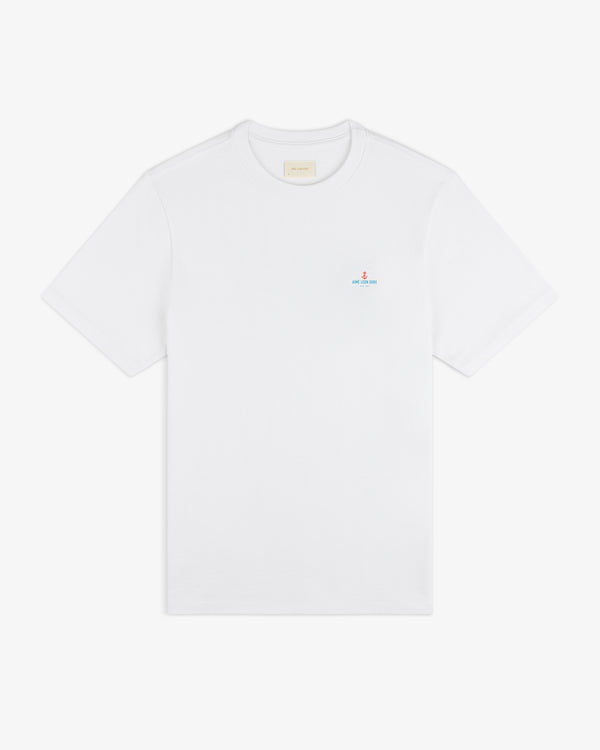 Coastal Flag Tee: white short-sleeve shirt with a small blue and red logo on the left chest.