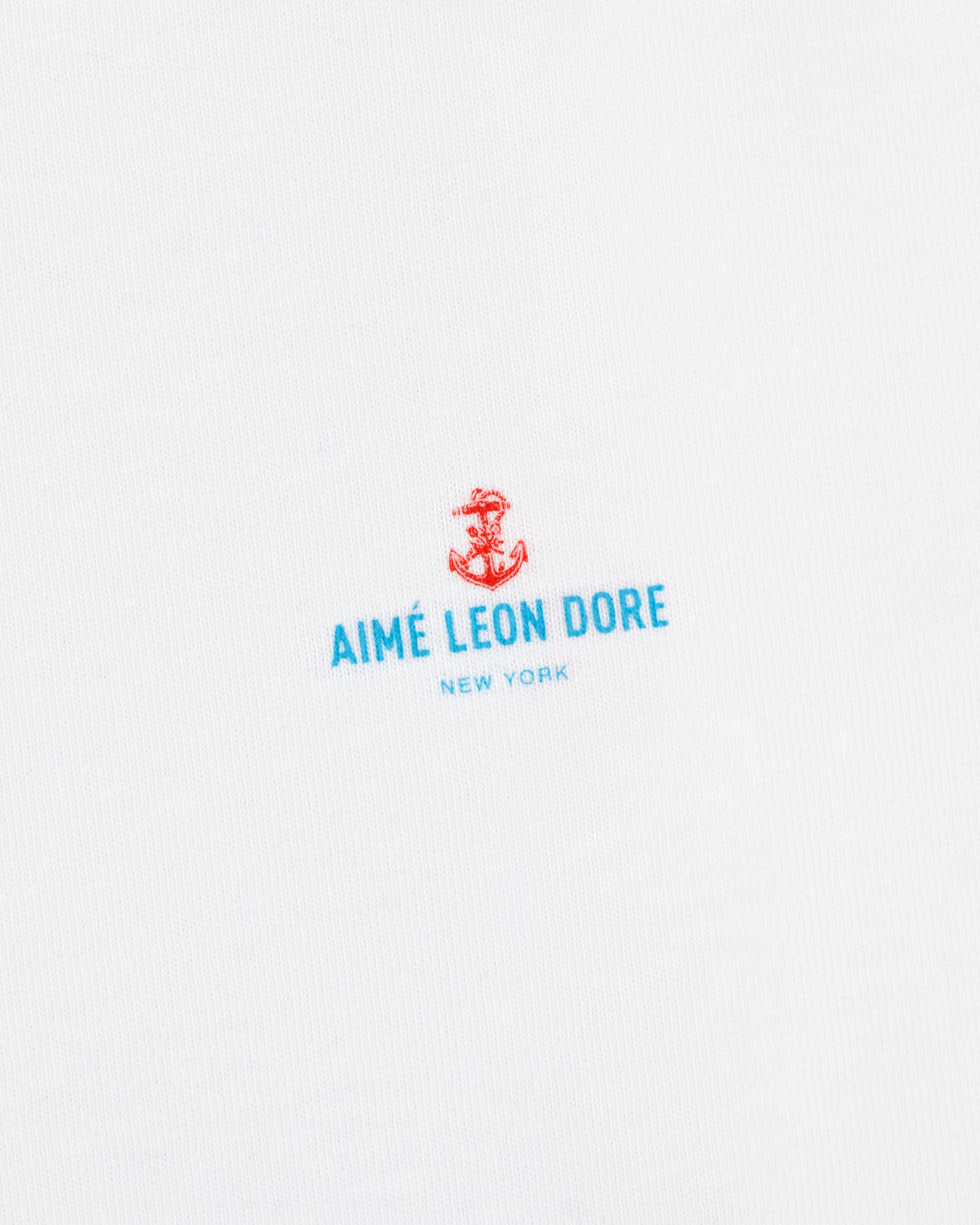White fabric with a small red anchor above blue "AIMÉ LEON DORE NEW YORK" text; Coastal Flag Tee.