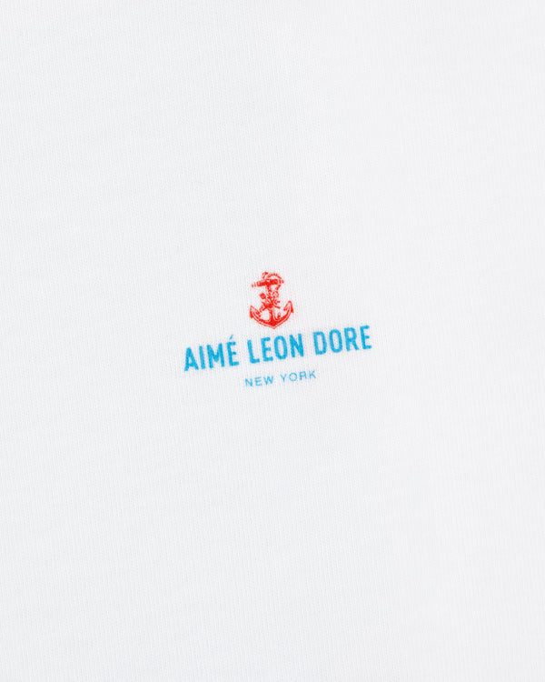 White fabric with a small red anchor above blue "AIMÉ LEON DORE NEW YORK" text; Coastal Flag Tee.