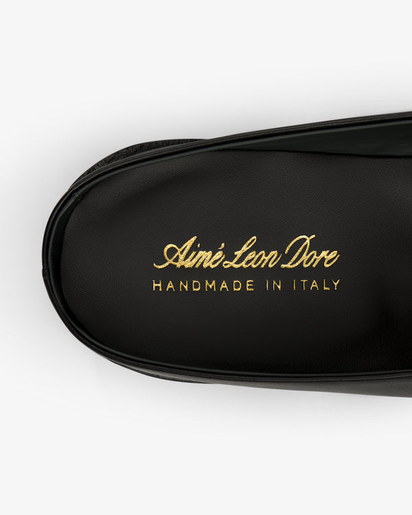 Black leather Venetian Mule with gold text reading Aimé Leon Dore HANDMADE IN ITALY embossed on it.