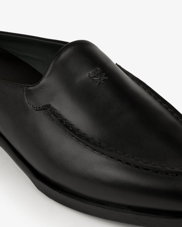 Close-up of the Venetian Mule, a black leather loafer with subtle stitching and a small embossed logo on the upper.
