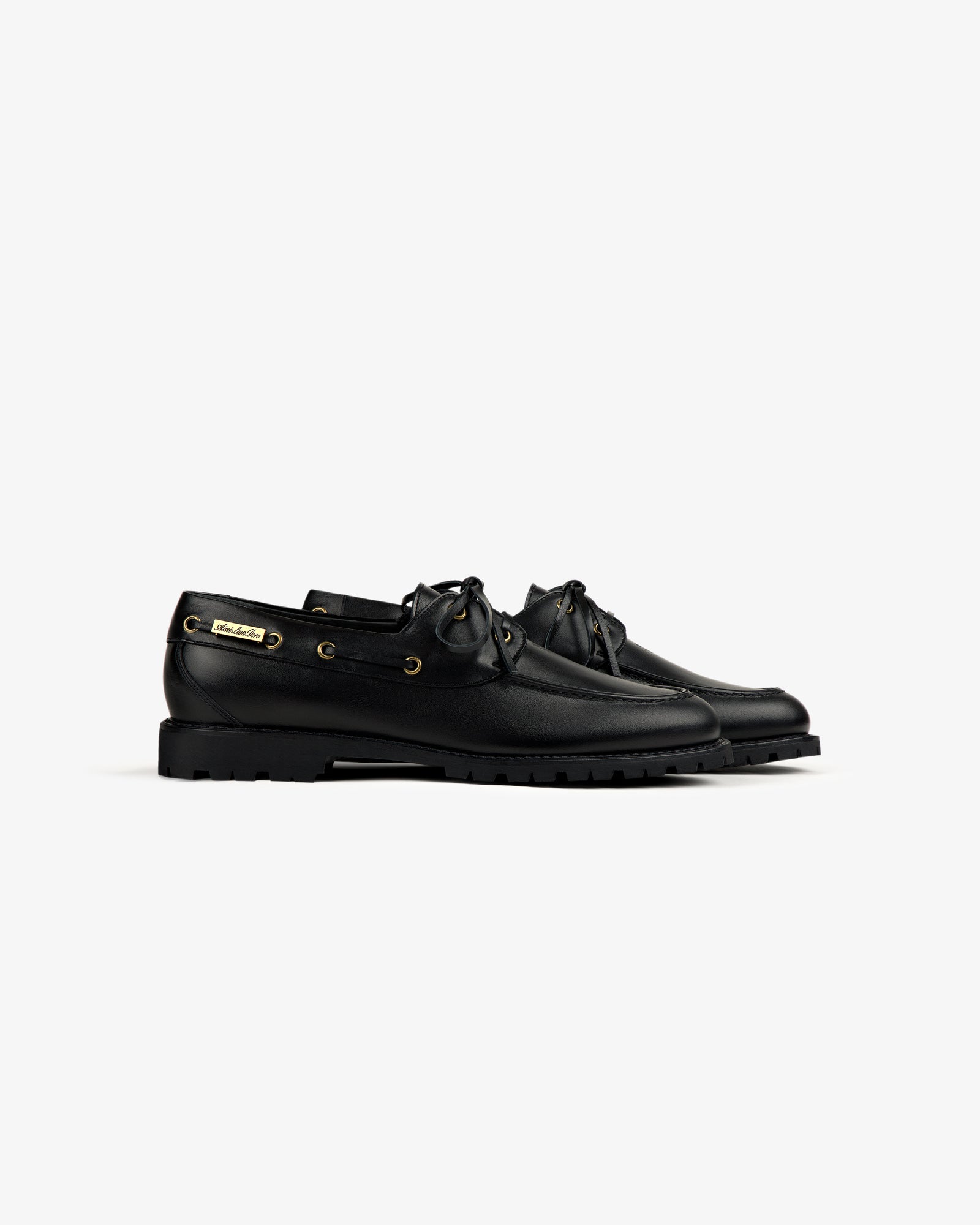 The Pápia Boat Shoe: black leather lace-up with gold eyelets and chunky rubber soles, shown on a white background.