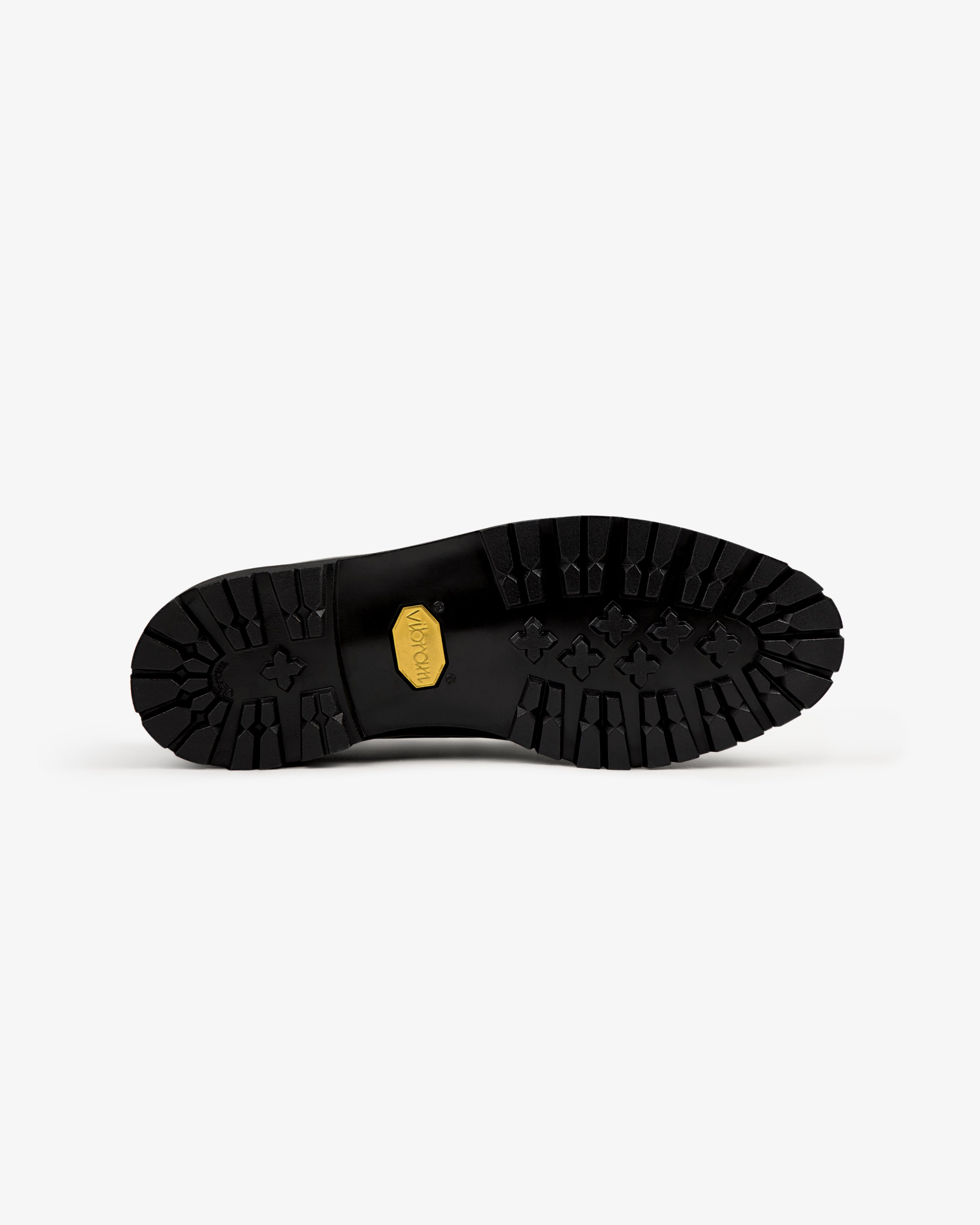 The Pápia Boat Shoe’s black sole features deep treads and a yellow Vibram logo, shown from beneath on white.