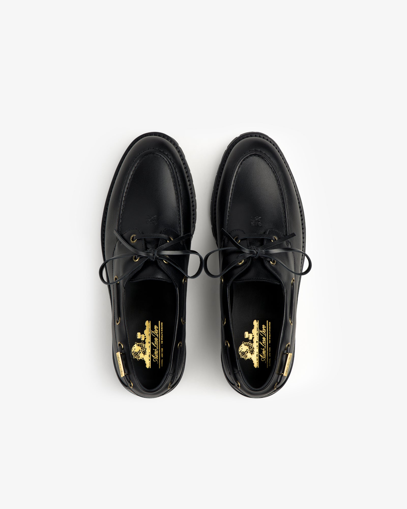 The Pápia Boat Shoe is a black leather lace-up shoe with gold logo details on the insoles, seen from above.