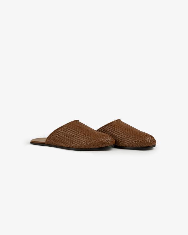 Leather Raffia Mule: brown woven slip-on with closed toe, flat sole, and open heel on a white background.