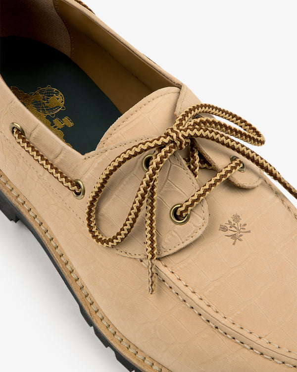 Pápia Boat Shoe: Beige leather with textured pattern, brown laces, gold eyelets, and embossed logo near laces.