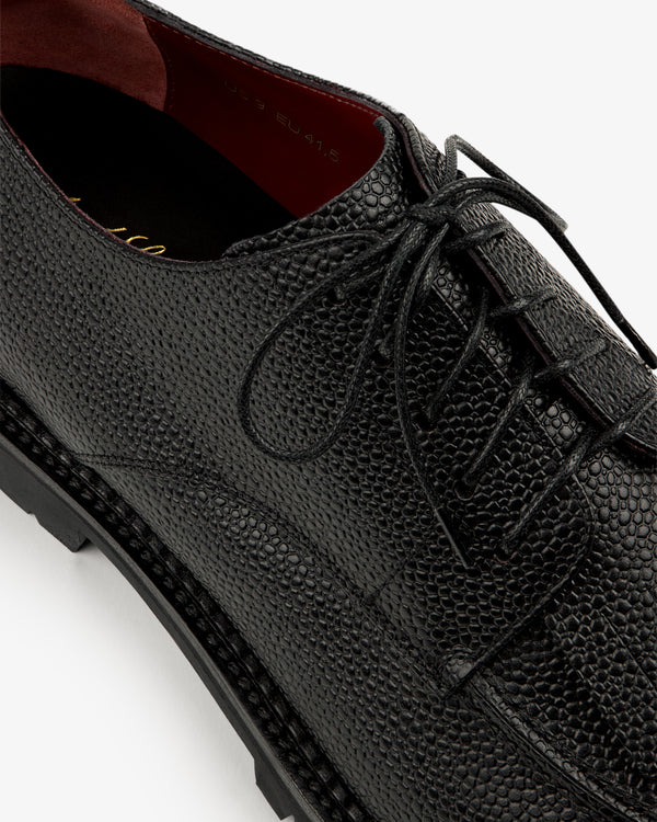 Close-up of the Leather Lug Sole Derby in black textured leather with laces and a rugged sole on a white background.