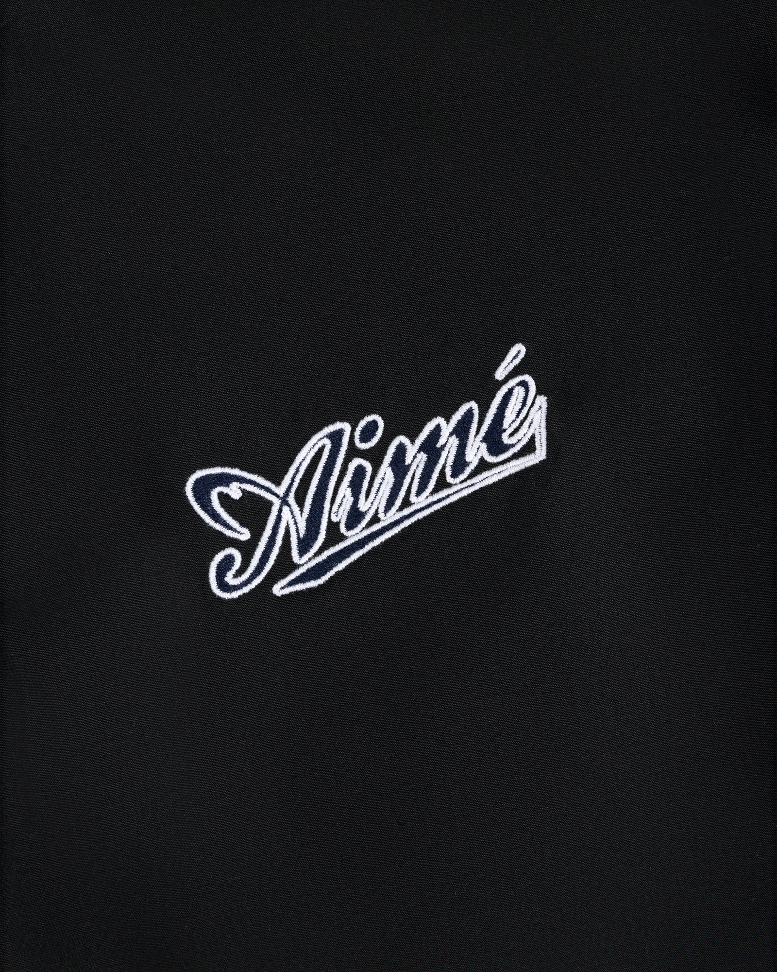 White Aimé script embroidered on black fabric of the Reversible Knit Bomber Jacket.