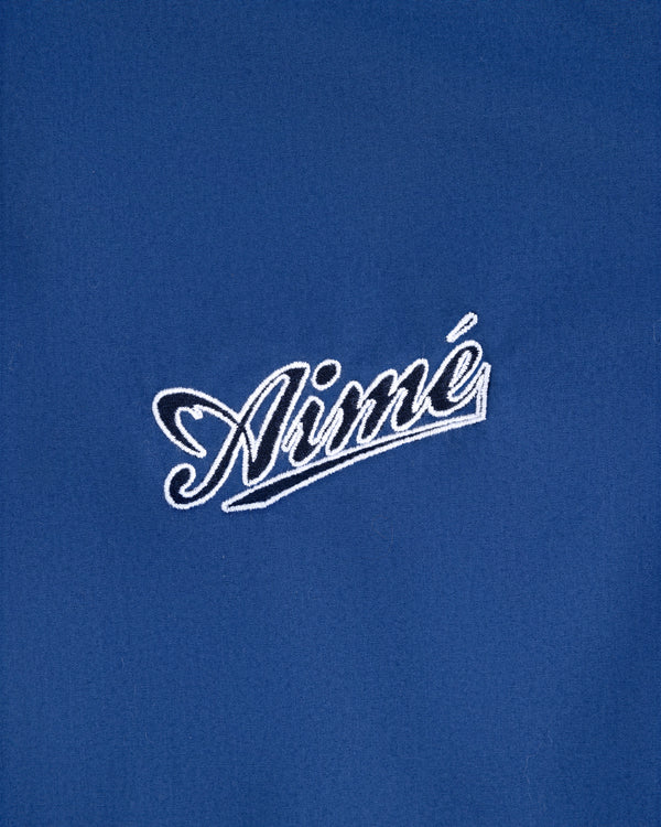 White cursive Aimé is embroidered on blue fabric of the Reversible Knit Bomber Jacket.
