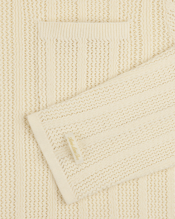 Close-up of the Racking Stitch Crewneck Sweater, a cream knit with a chest pocket and Alabama Blue tag on the sleeve.