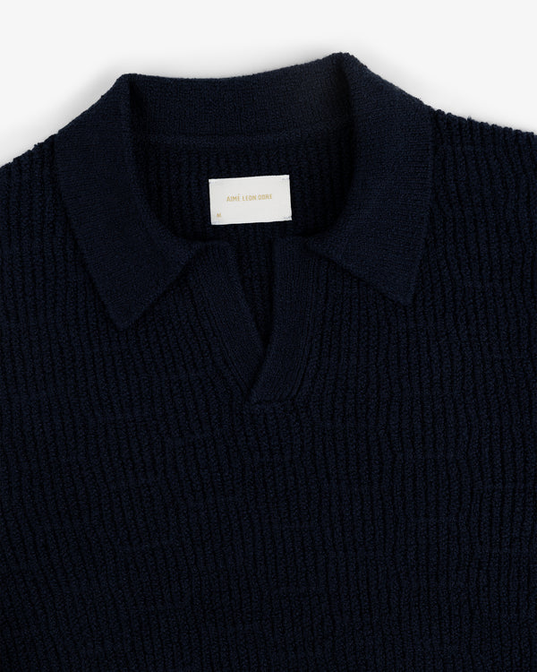 The Long-Sleeve Boucle Polo is a navy ribbed knit shirt with a collar and a small white label at the neckline.
