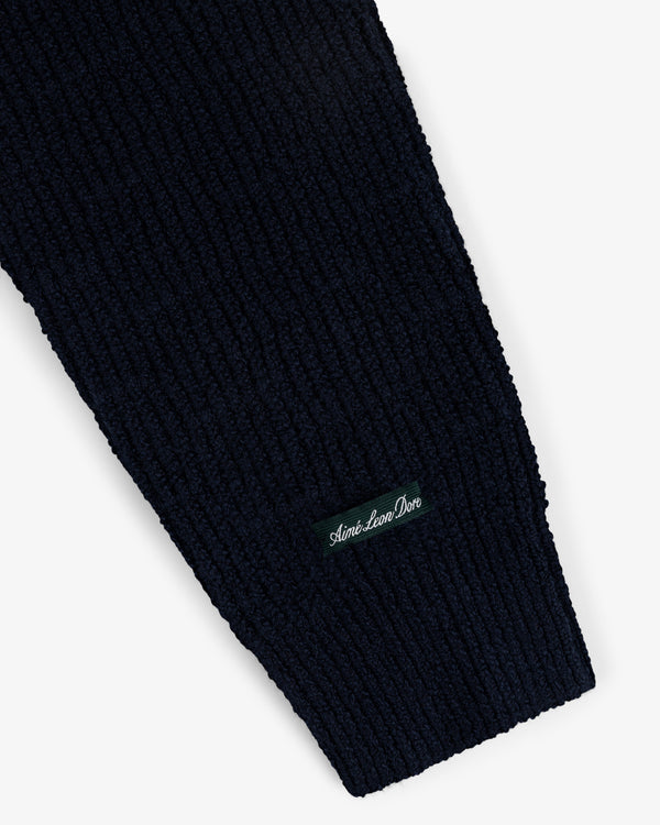 Close-up of a ribbed navy sleeve from the Long-Sleeve Boucle Polo, featuring a black Aimé Leon Dore patch in white.