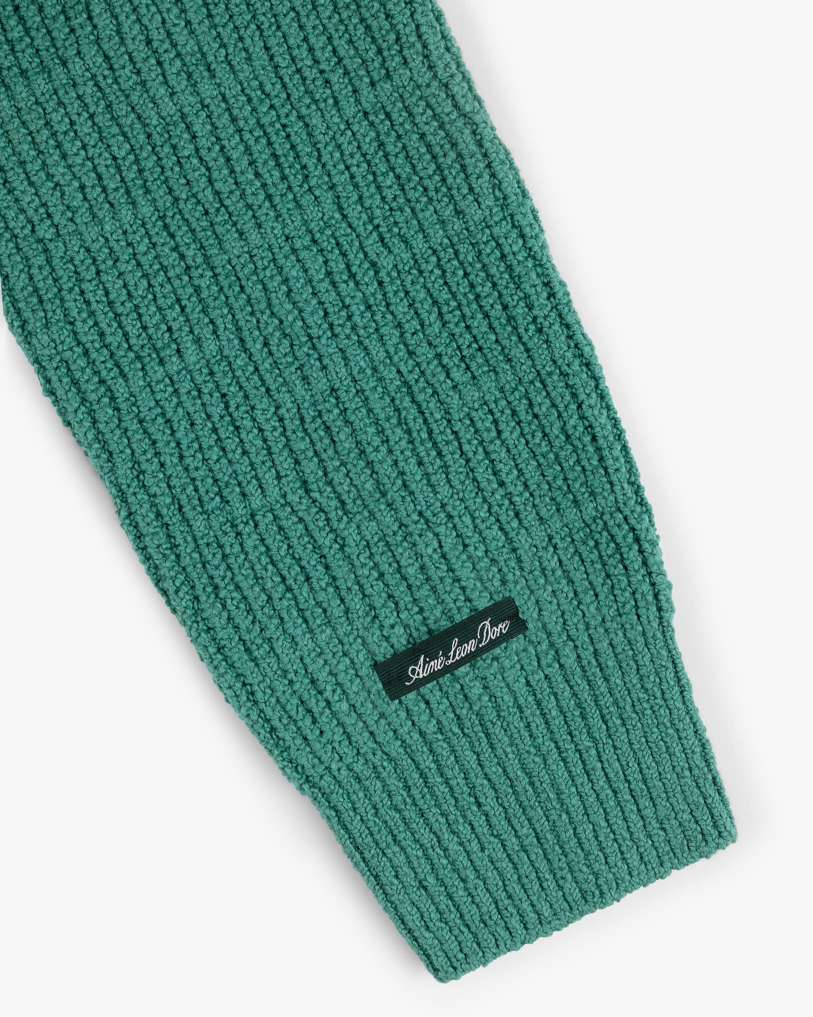 Close-up of a green Long-Sleeve Boucle Polo's ribbed knit sleeve with a small black Aimé Leon Dore label.