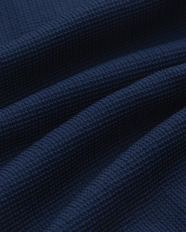 Close-up of Knit Polo in dark blue, featuring a textured waffle weave and gentle, wavy folds.